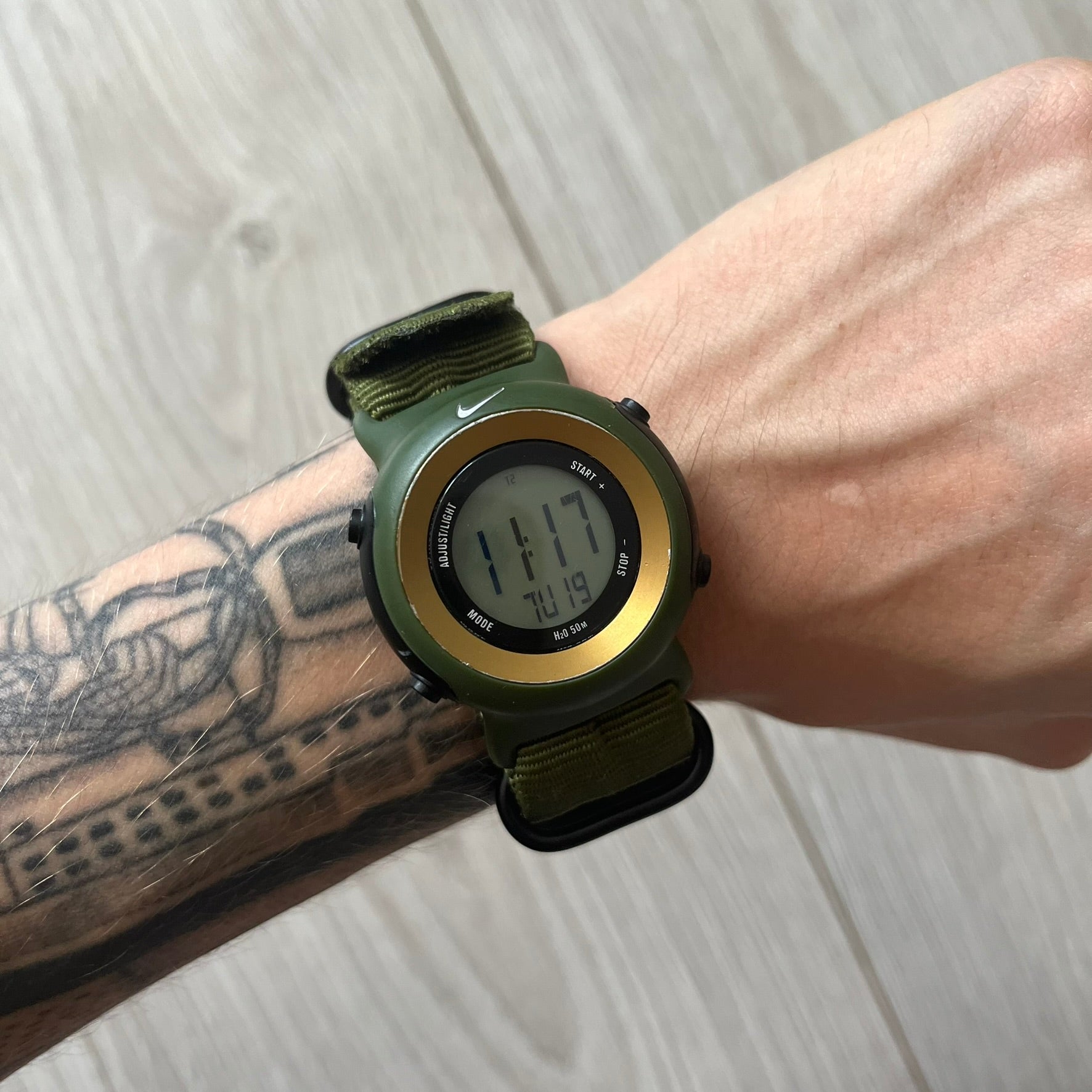 Green digital watch on a wrist with tattoos against a light wooden background