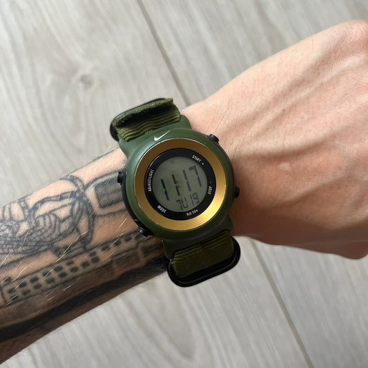 Green digital watch on a wrist with tattoos against a light wooden background