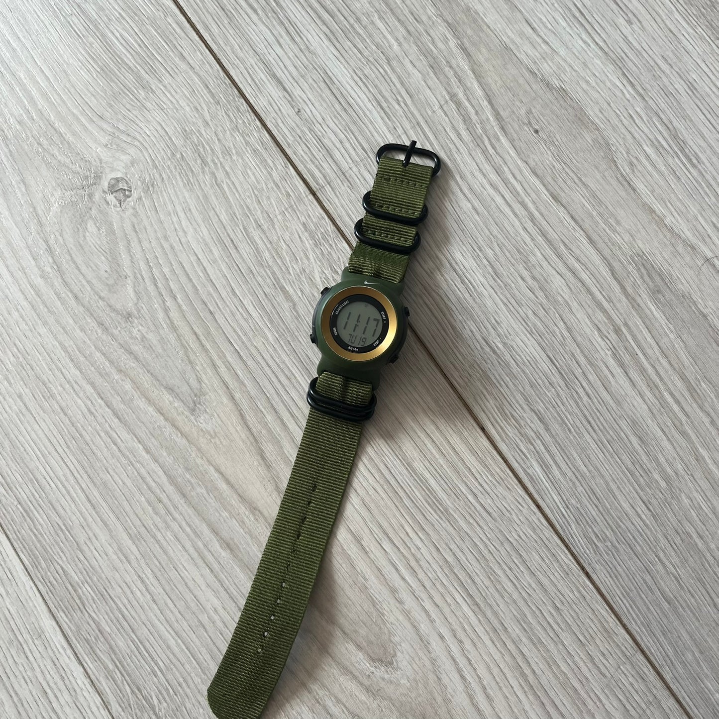 Green watch with a metal face on a light wooden surface