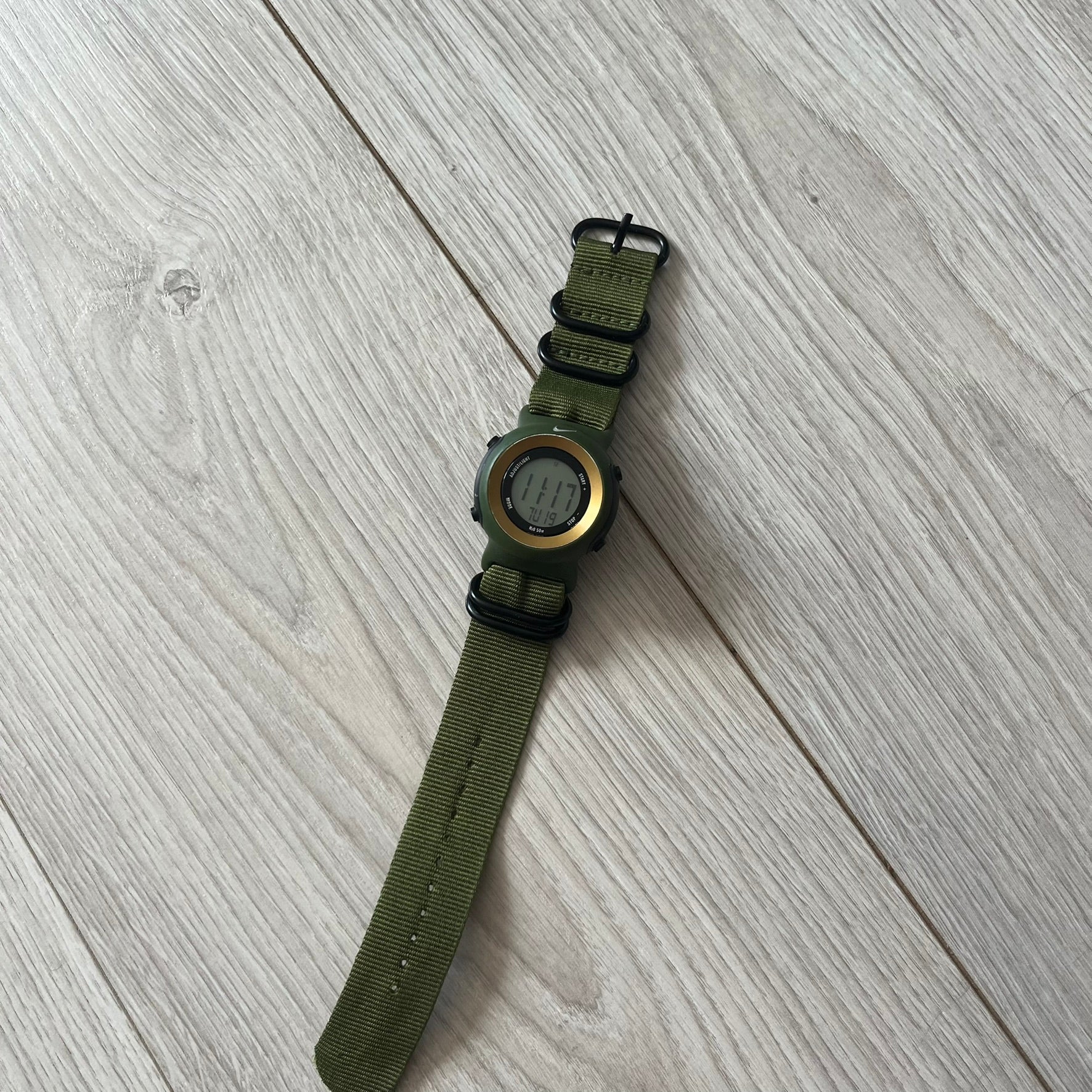 Green watch with a metal face on a light wooden surface