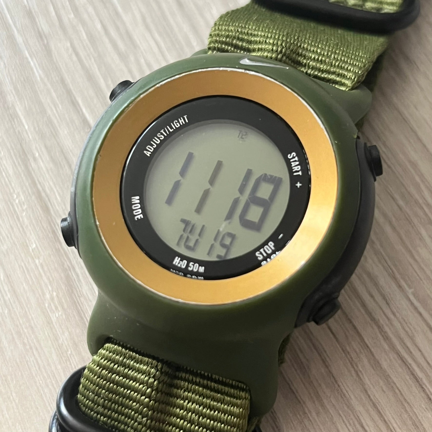 Green digital watch with a gold bezel on a wooden surface