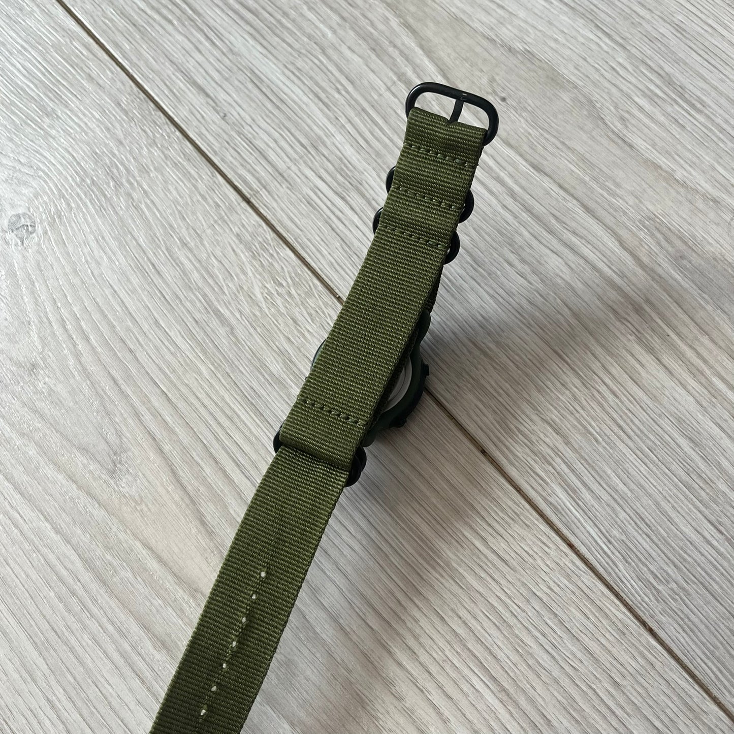 Green watch strap on a light wooden surface