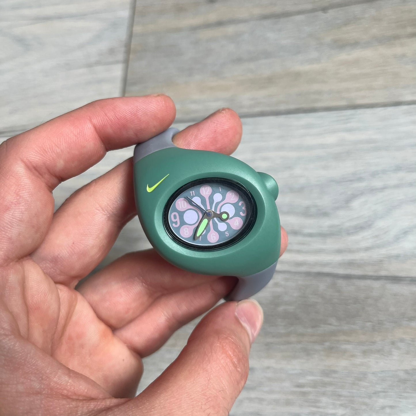 Nike Triax Junior WR0033-401 Fog Blue Analog Watch is a 2000's analog watch featuring a Turquoise case with a small light green Nike logo above the dial. The face is purple and pink with bubbles effect, paired with green hands and pink numerals. It is fitted with gray blue straps. Constructed from stainless steel and plastic materials, the watch is water resistant up to 50 meters. Comes with a tag and rare plastic box.