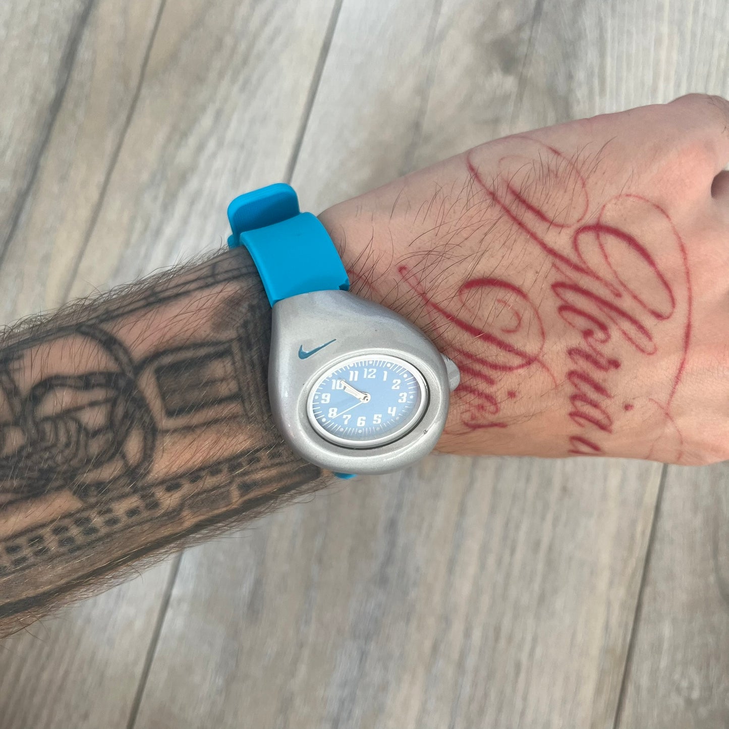 Nike Triax Junior WR0033 Blue Analog Watch is a 2000's analog watch featuring a silver-tone case with a small blue Nike logo above the dial. The light blue face is paired with white hands and white numerals for contrast. It is fitted with blue replacement straps that are not original Nike straps. Constructed from stainless steel and plastic materials, the watch is water resistant up to 50 meters and includes US patent markings.