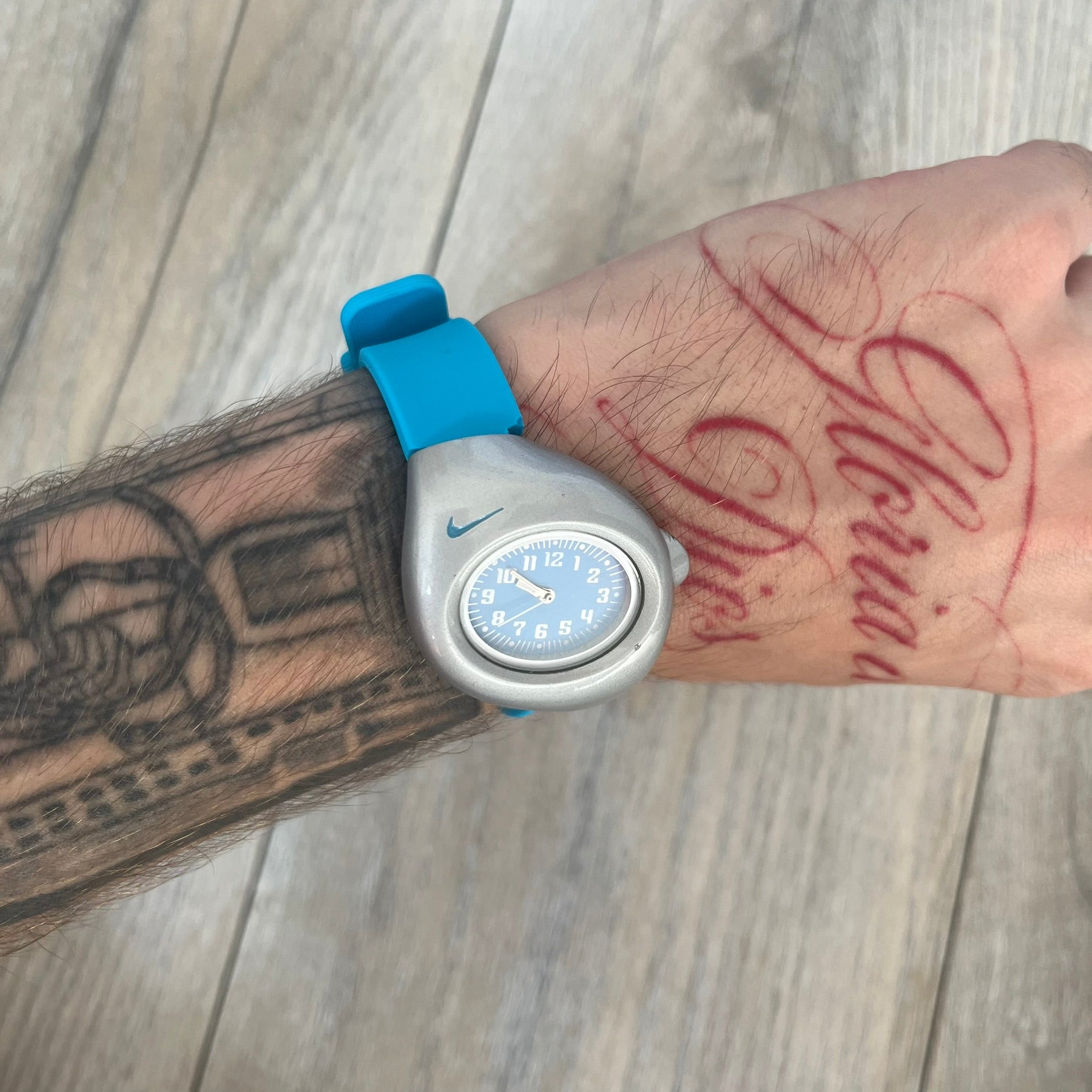 Nike Triax Junior WR0033 Blue Analog Watch is a 2000's analog watch featuring a silver-tone case with a small blue Nike logo above the dial. The light blue face is paired with white hands and white numerals for contrast. It is fitted with blue replacement straps that are not original Nike straps. Constructed from stainless steel and plastic materials, the watch is water resistant up to 50 meters and includes US patent markings.