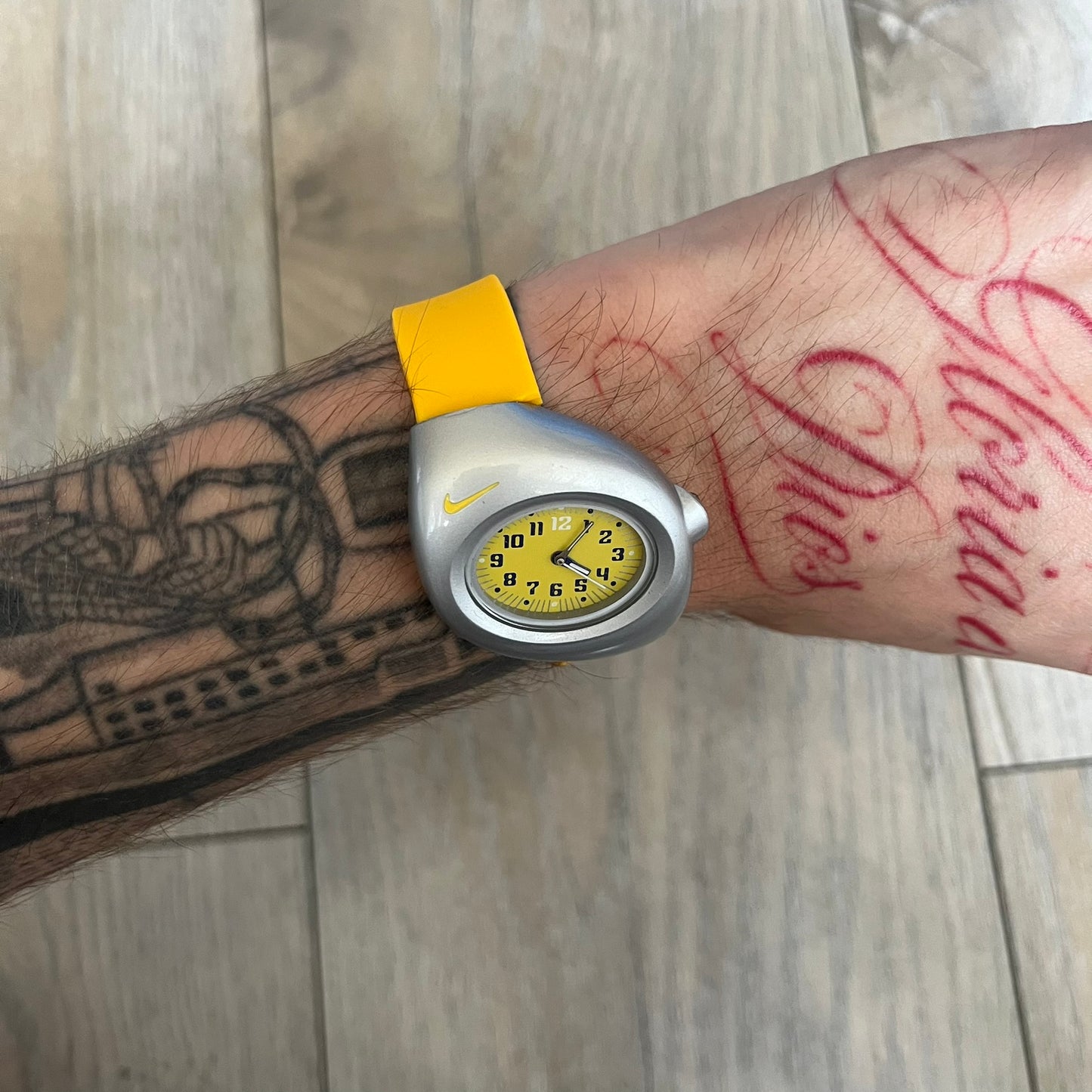 Nike Triax Junior WR0033 Yellow Analog Watch is a 2000s analog watch featuring a silver-tone case with a small yellow Nike logo above the dial. The yellow face is paired with white hands and white-and-black numerals for contrast. It is fitted with yellow replacement straps that are not original Nike straps. Constructed from stainless steel and plastic materials, the watch is water resistant up to 50 meters and includes US patent markings.