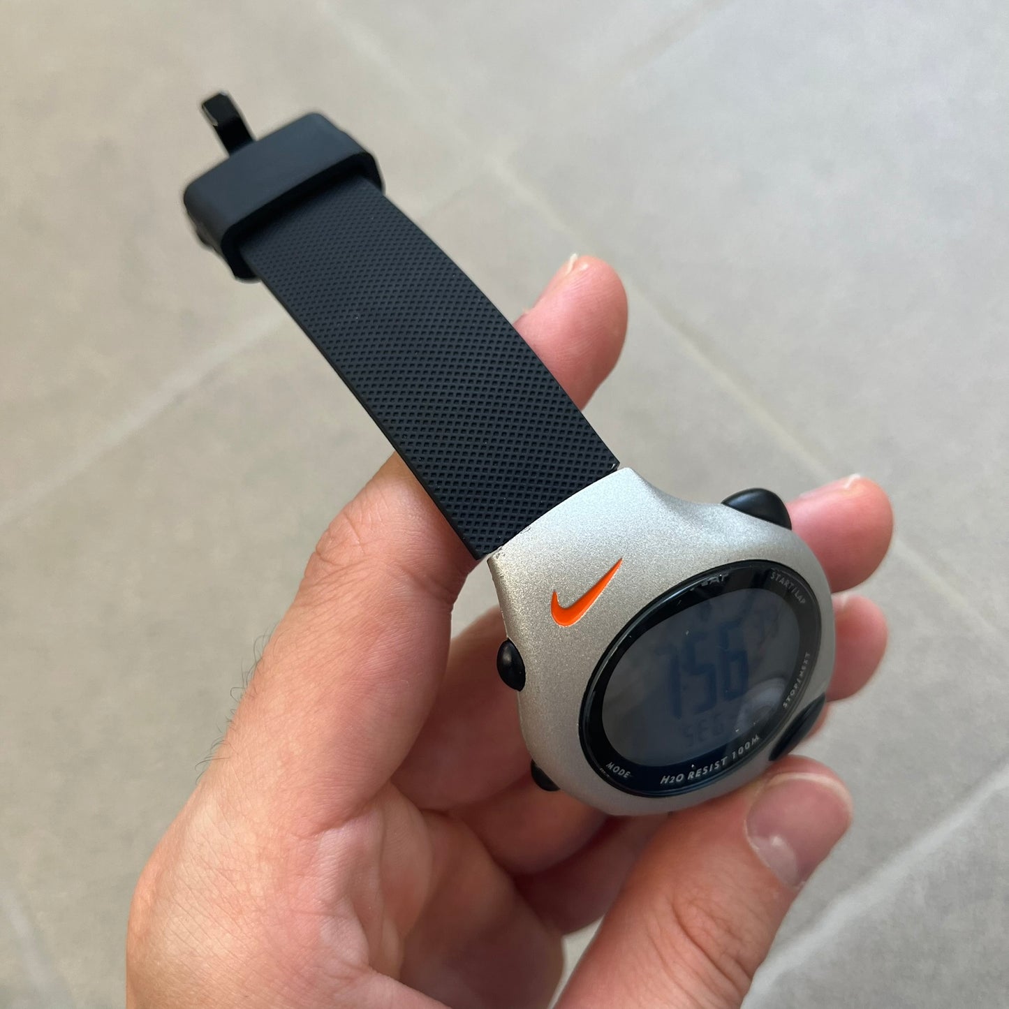 Nike Triax Regular 20 Silver Analog Watch features a silver-tone case with four black side buttons and a front button for the backlight function. The watch has an orange Nike Swoosh on the top of the case, 20-lap memory, multiple modes, and 100m water resistance. It comes with black replacement straps that are not original Nike.
