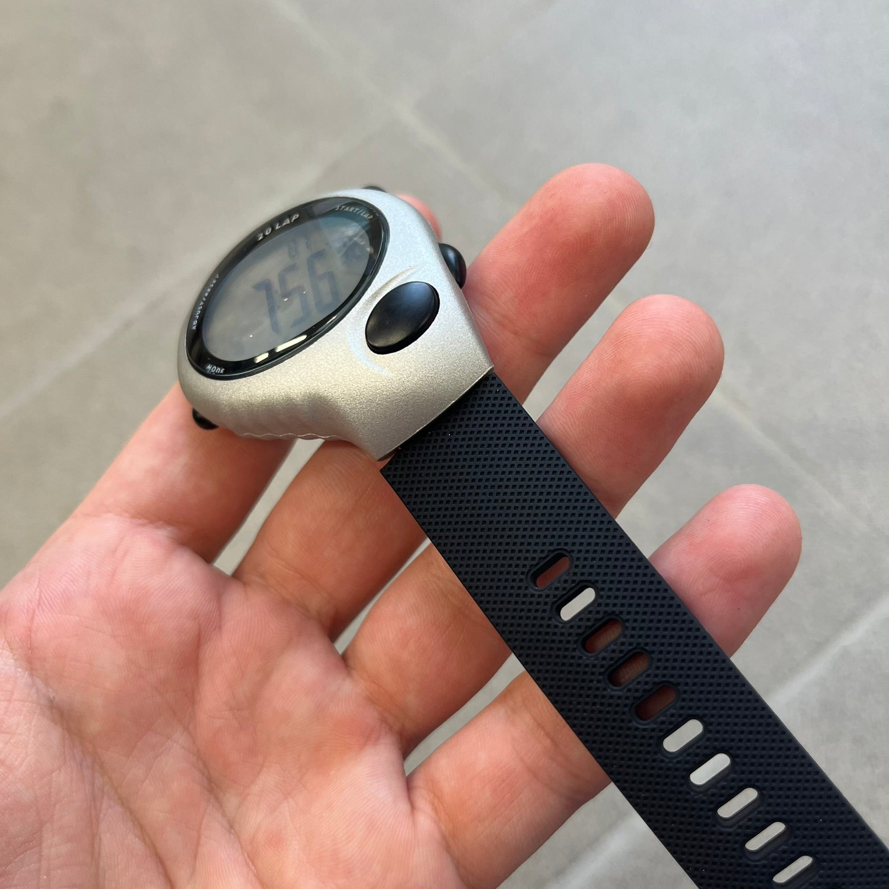 Nike Triax Regular 20 Silver Analog Watch features a silver-tone case with four black side buttons and a front button for the backlight function. The watch has an orange Nike Swoosh on the top of the case, 20-lap memory, multiple modes, and 100m water resistance. It comes with black replacement straps that are not original Nike.
