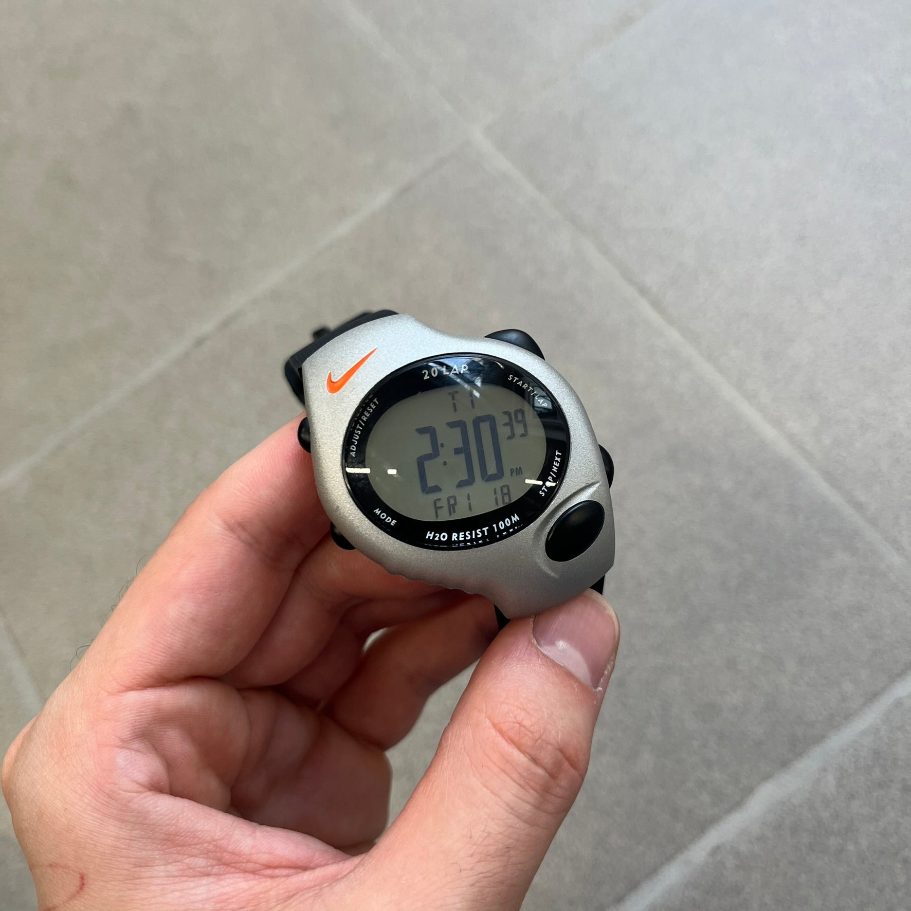 Nike Triax Regular 20 Silver Analog Watch features a silver-tone case with four black side buttons and a front button for the backlight function. The watch has an orange Nike Swoosh on the top of the case, 20-lap memory, multiple modes, and 100m water resistance. It comes with black replacement straps that are not original Nike.
