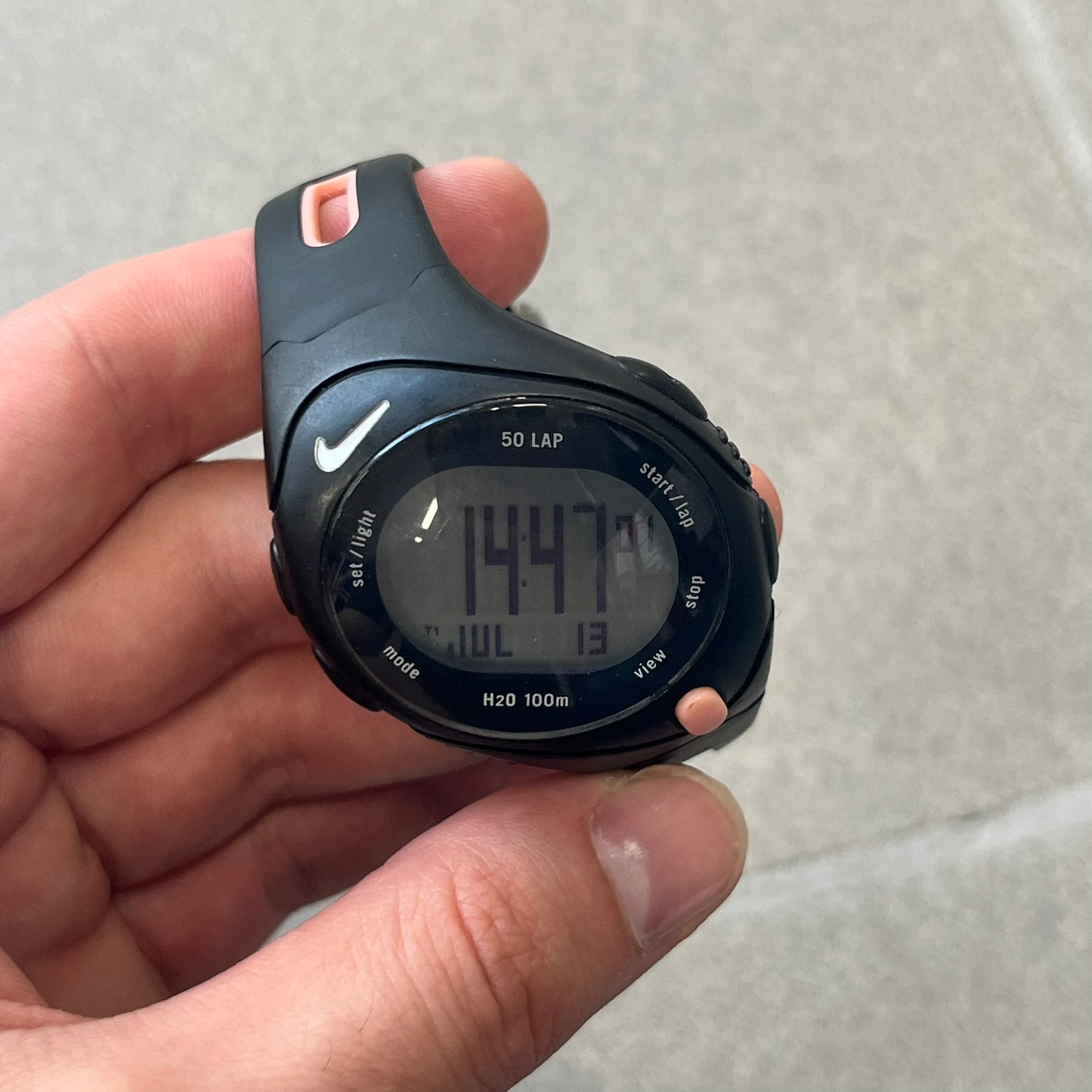 Nike Triax Speed 50 Regular Pink Digital Watch features a black case with four black side buttons and a pink-ish front button for the backlight function. The watch has an white Nike Swoosh on the top of the case, 50-lap memory, multiple modes, and 100m water resistance.