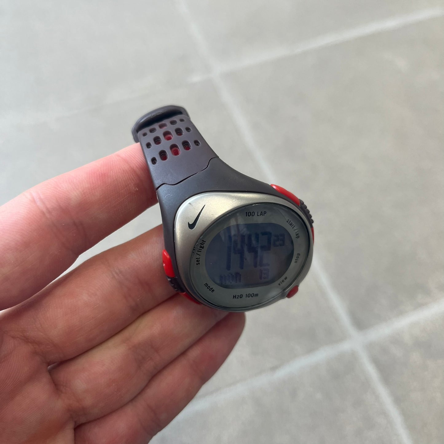 Nike Triax Speed 100 Regular Red Digital Watch features a silver-tone case with four red side buttons and a front button for the backlight function. The watch has an black Nike Swoosh on the top of the case, 100-lap memory, multiple modes, and 100m water resistance. It comes with brown-ish bracelet.
