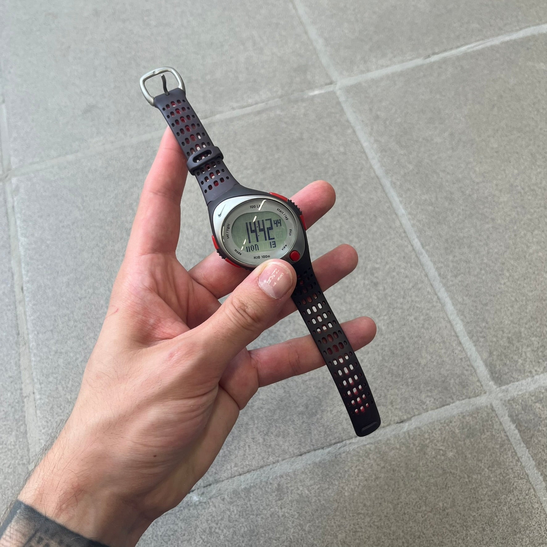 Nike Triax Speed 100 Regular Red Digital Watch features a silver-tone case with four red side buttons and a front button for the backlight function. The watch has an black Nike Swoosh on the top of the case, 100-lap memory, multiple modes, and 100m water resistance. It comes with brown-ish bracelet.
