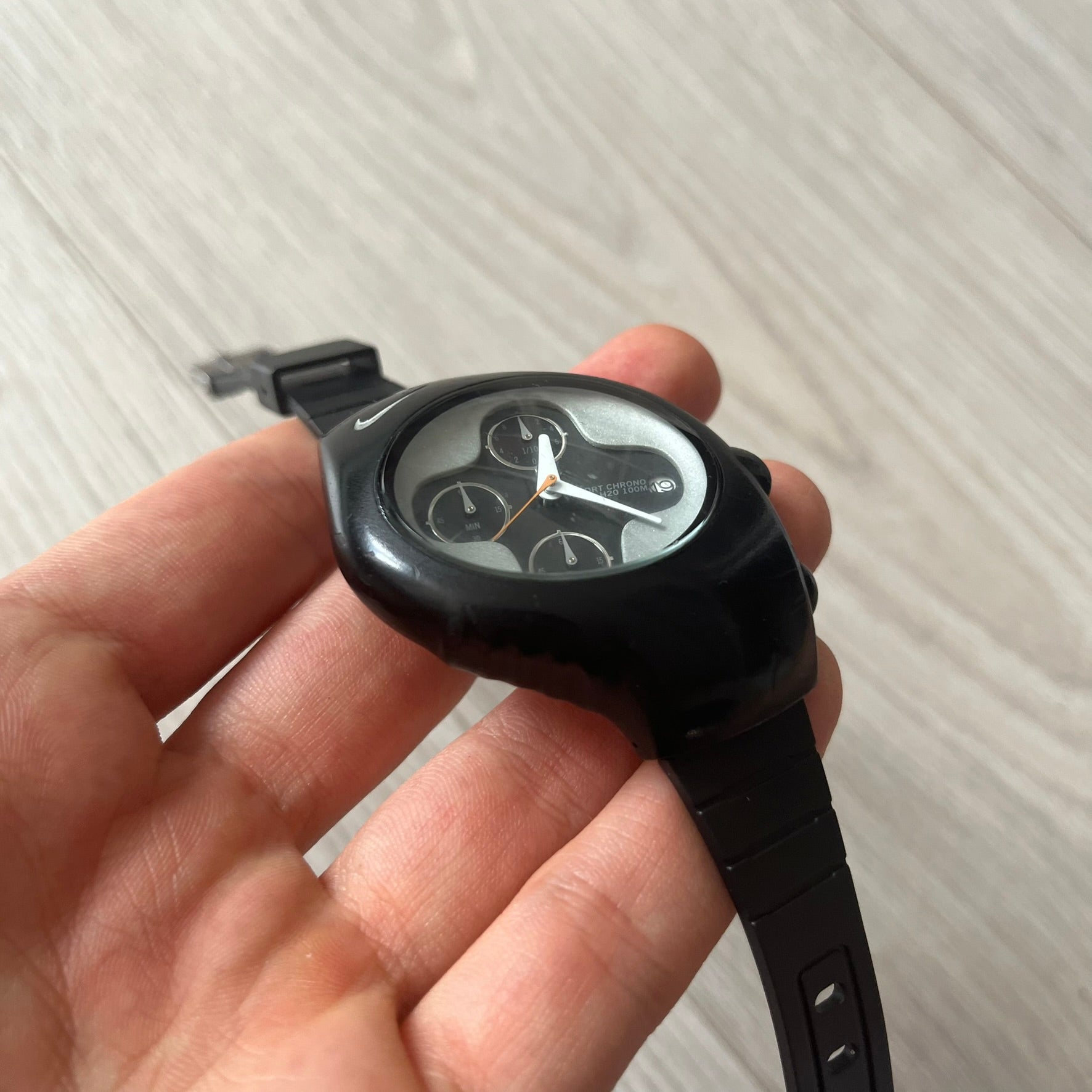 Black wristwatch held in a hand against a light background