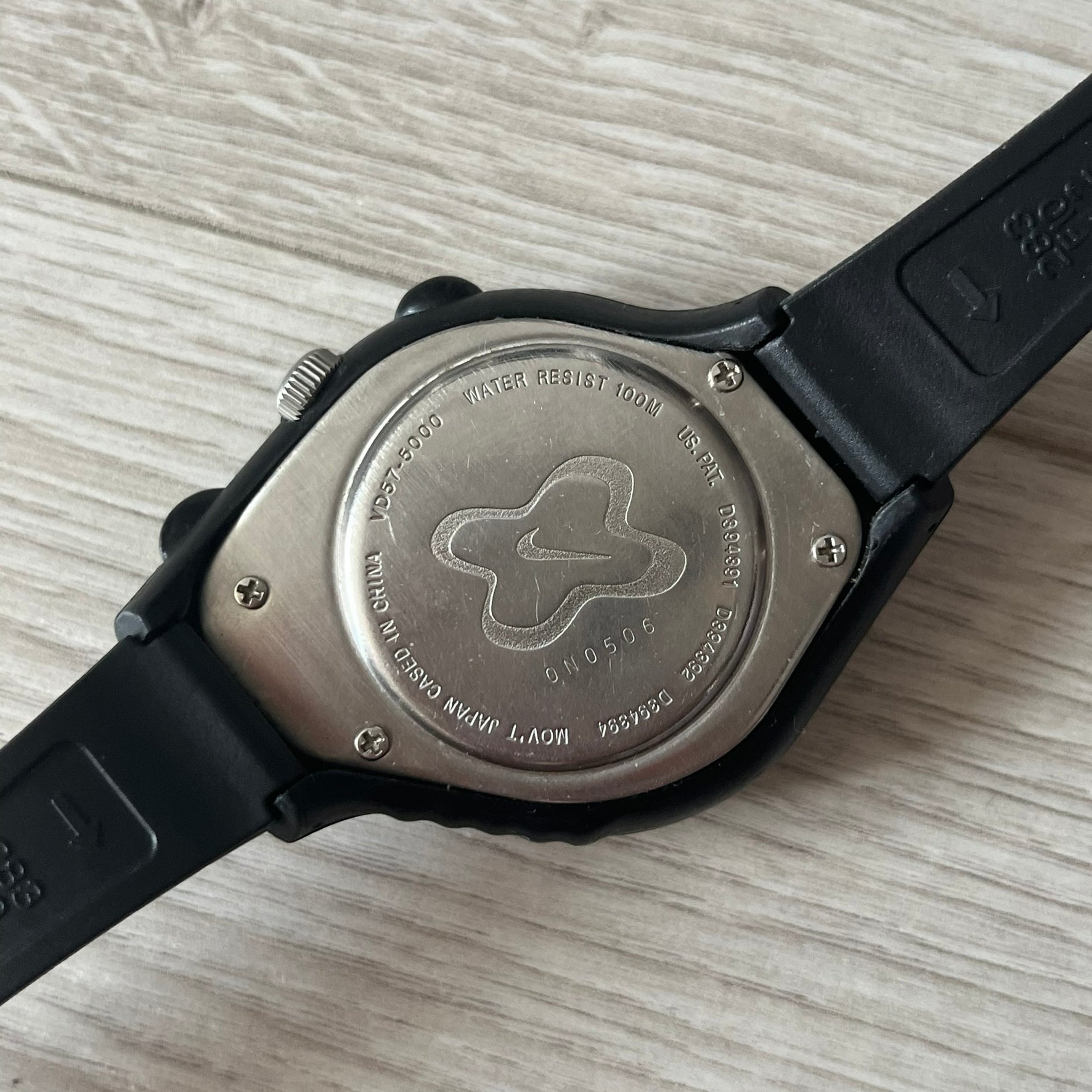 Back view of a watch with brand engraving on a light wooden surface
