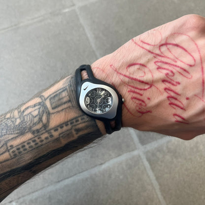Nike Triax Sweeper is a really small analog watch that features a compact silver-tone case with a black Nike Swoosh at the top. It has black rubber straps and a black dial with white hour markers and decorative star and dot graphics. The watch is water resistant to 50 metres.