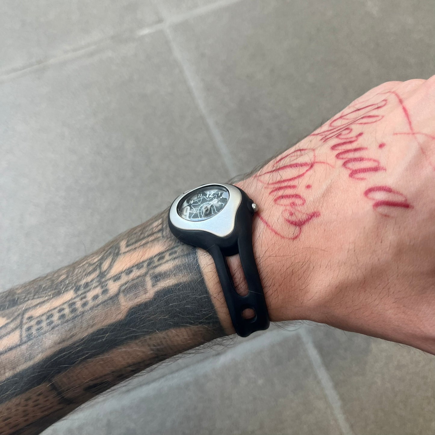 Nike Triax Sweeper is a really small analog watch that features a compact silver-tone case with a black Nike Swoosh at the top. It has black rubber straps and a black dial with white hour markers and decorative star and dot graphics. The watch is water resistant to 50 metres.