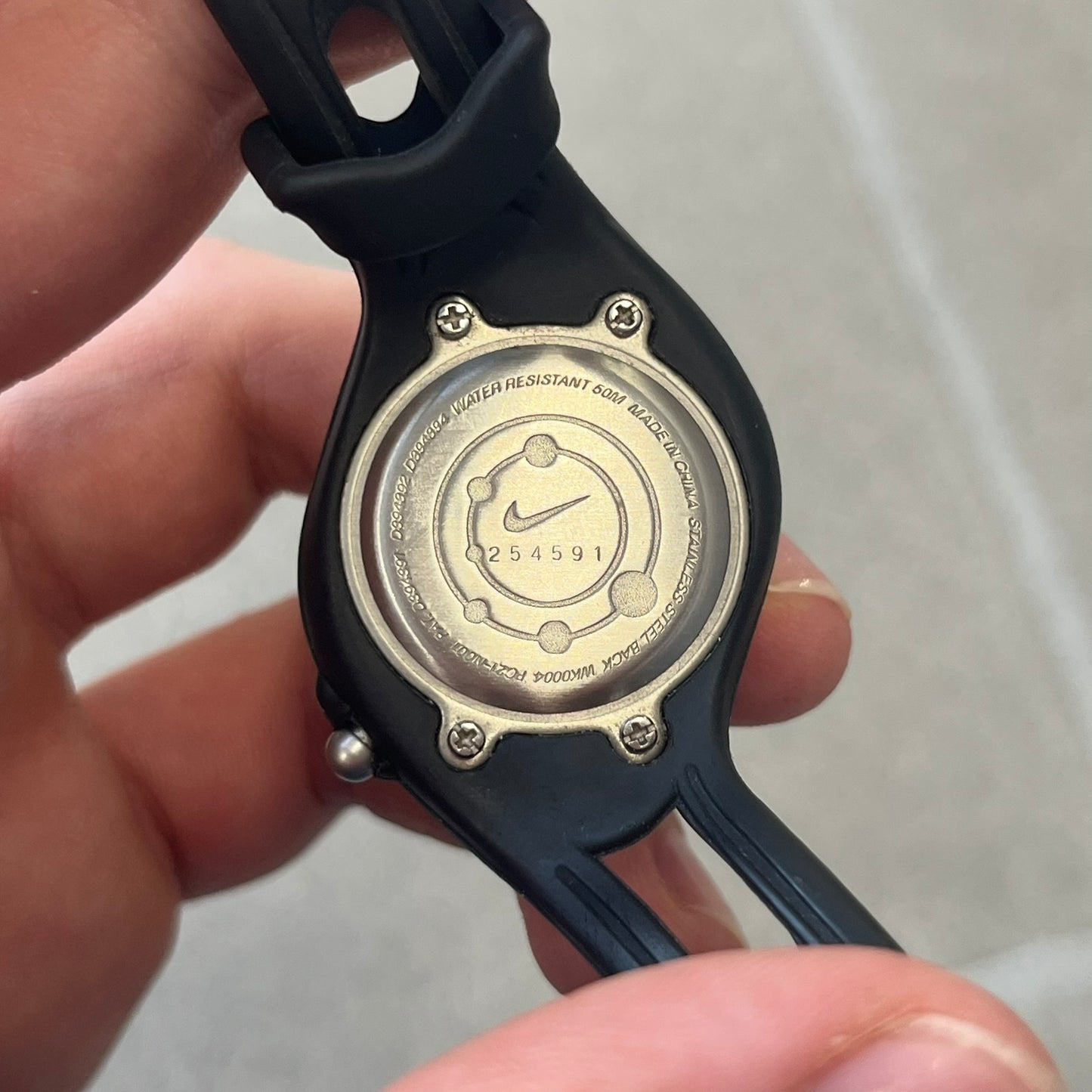 Nike Triax Sweeper is a really small analog watch that features a compact silver-tone case with a black Nike Swoosh at the top. It has black rubber straps and a black dial with white hour markers and decorative star and dot graphics. The watch is water resistant to 50 metres.