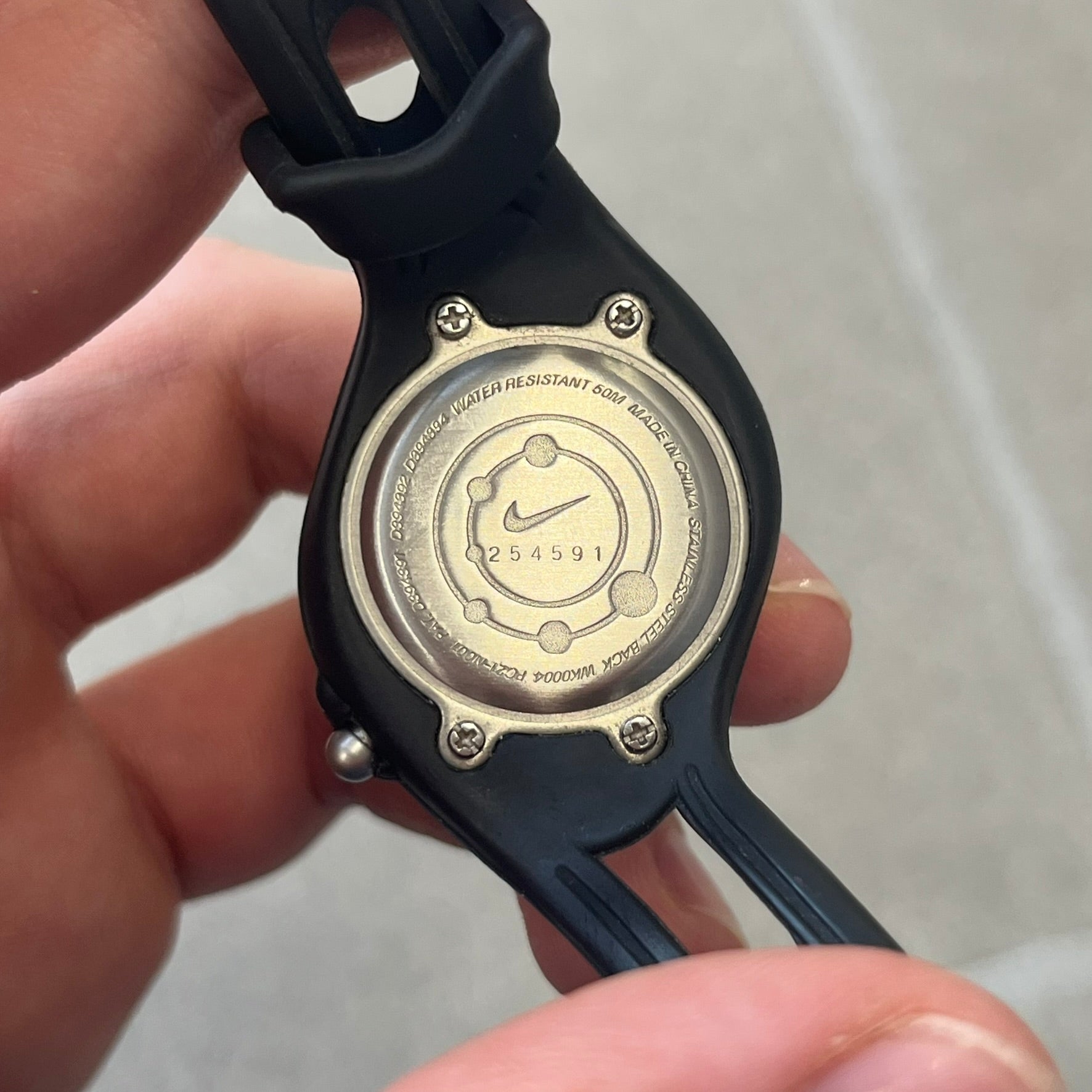 Nike Triax Sweeper is a really small analog watch that features a compact silver-tone case with a black Nike Swoosh at the top. It has black rubber straps and a black dial with white hour markers and decorative star and dot graphics. The watch is water resistant to 50 metres.