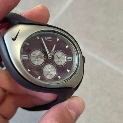 Nike Triax Swift 3i Burgundy WR0091 Analog Watch comes with burgundy and red rubber straps and a silver case featuring a dark Nike Swoosh. The burgundy metallic dial has a dotted pattern, three silver subdials for day, date, and hour and silver hands. Seconds markings are printed on the inner edge of the case and are visible only at an angle.
