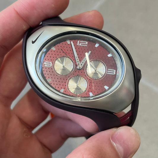 Nike Triax Swift 3i Burgundy WR0091 Analog Watch comes with burgundy and red rubber straps and a silver case featuring a dark Nike Swoosh. The burgundy metallic dial has a dotted pattern, three silver subdials for day, date, and hour and silver hands. Seconds markings are printed on the inner edge of the case and are visible only at an angle.