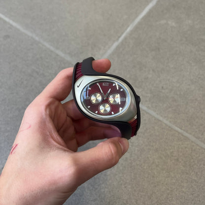 Nike Triax Swift 3i Burgundy WR0091 Analog Watch comes with burgundy and red rubber straps and a silver case featuring a dark Nike Swoosh. The burgundy metallic dial has a dotted pattern, three silver subdials for day, date, and hour and silver hands. Seconds markings are printed on the inner edge of the case and are visible only at an angle.