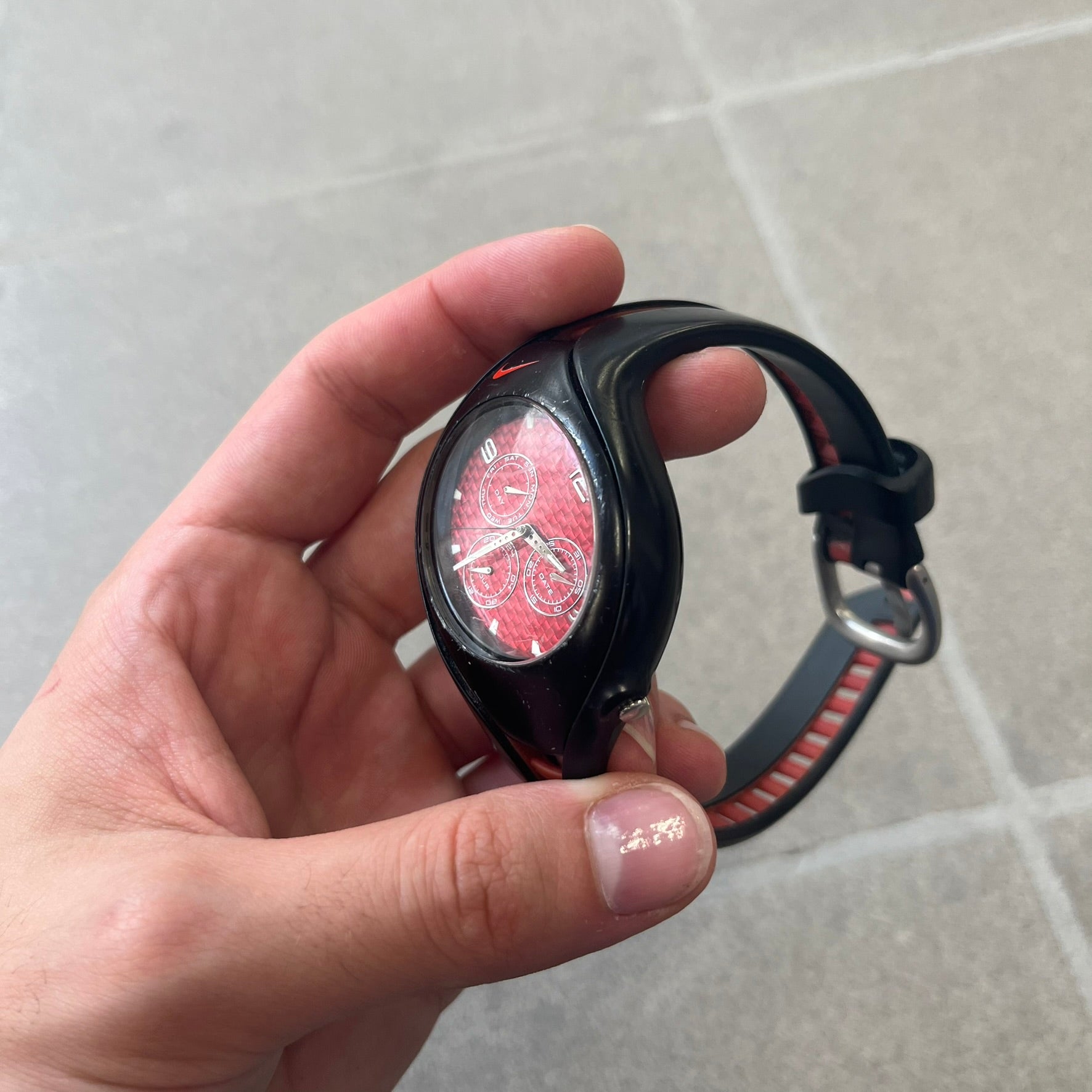 Nike Triax Swift 3i Red WR0091 Analog Watch comes with black &amp; red rubber straps and a black case featuring a red Nike Swoosh. The red metallic dial has a woven pattern, three silver subdials for day, date, and hour and silver hands. Seconds markings are printed on the inner edge of the case and are visible only at an angle. Sport-focused Triax case design with water-resistant construction.