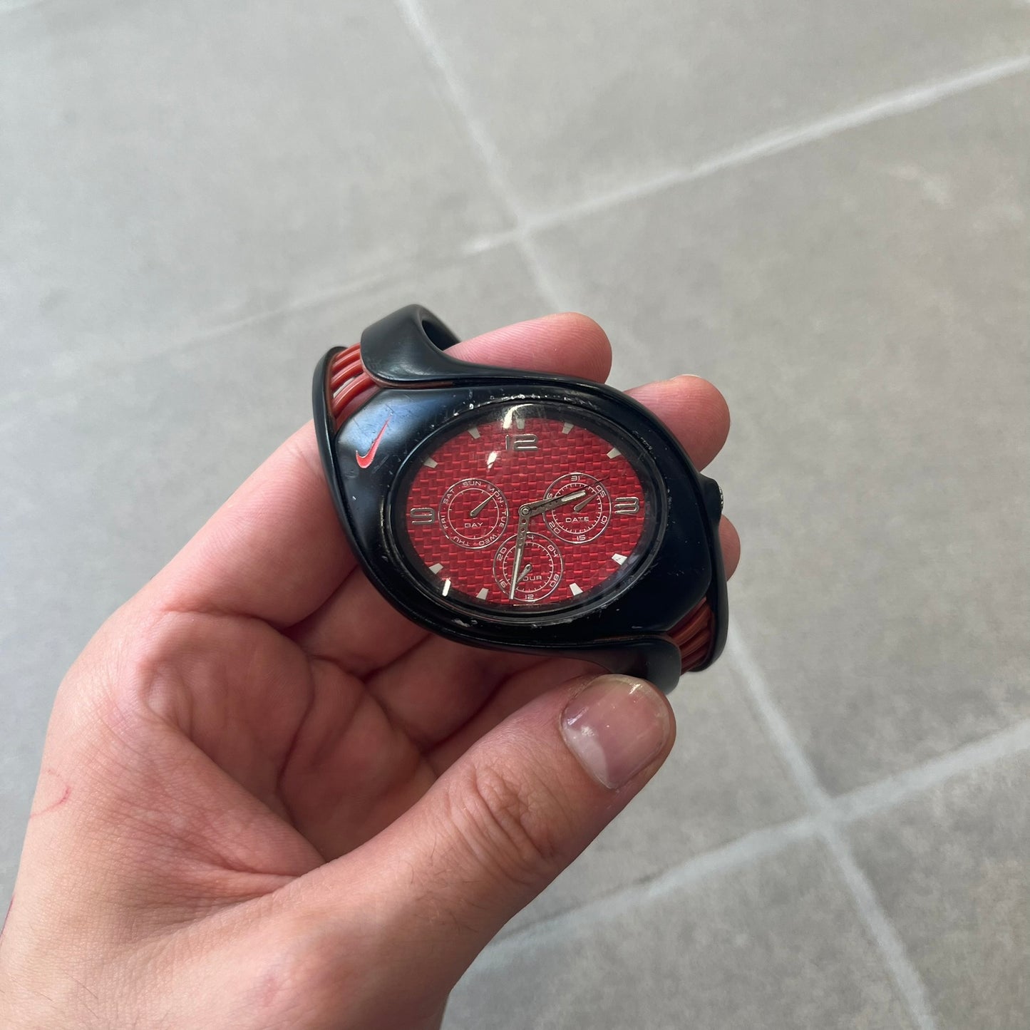 Nike Triax Swift 3i Red WR0091 Analog Watch comes with black &amp; red rubber straps and a black case featuring a red Nike Swoosh. The red metallic dial has a woven pattern, three silver subdials for day, date, and hour and silver hands. Seconds markings are printed on the inner edge of the case and are visible only at an angle. Sport-focused Triax case design with water-resistant construction.