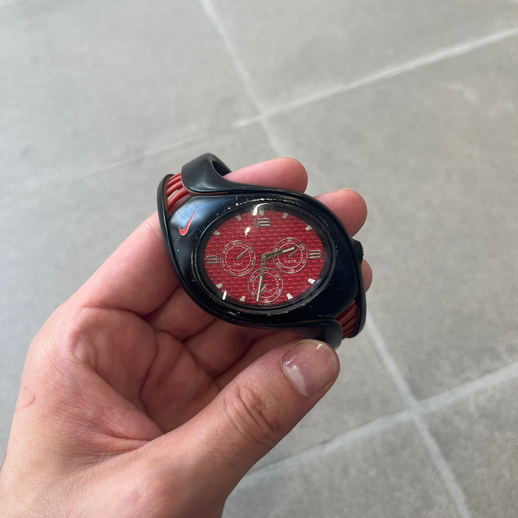Nike Triax Swift 3i Red WR0091 Analog Watch comes with black &amp; red rubber straps and a black case featuring a red Nike Swoosh. The red metallic dial has a woven pattern, three silver subdials for day, date, and hour and silver hands. Seconds markings are printed on the inner edge of the case and are visible only at an angle. Sport-focused Triax case design with water-resistant construction.
