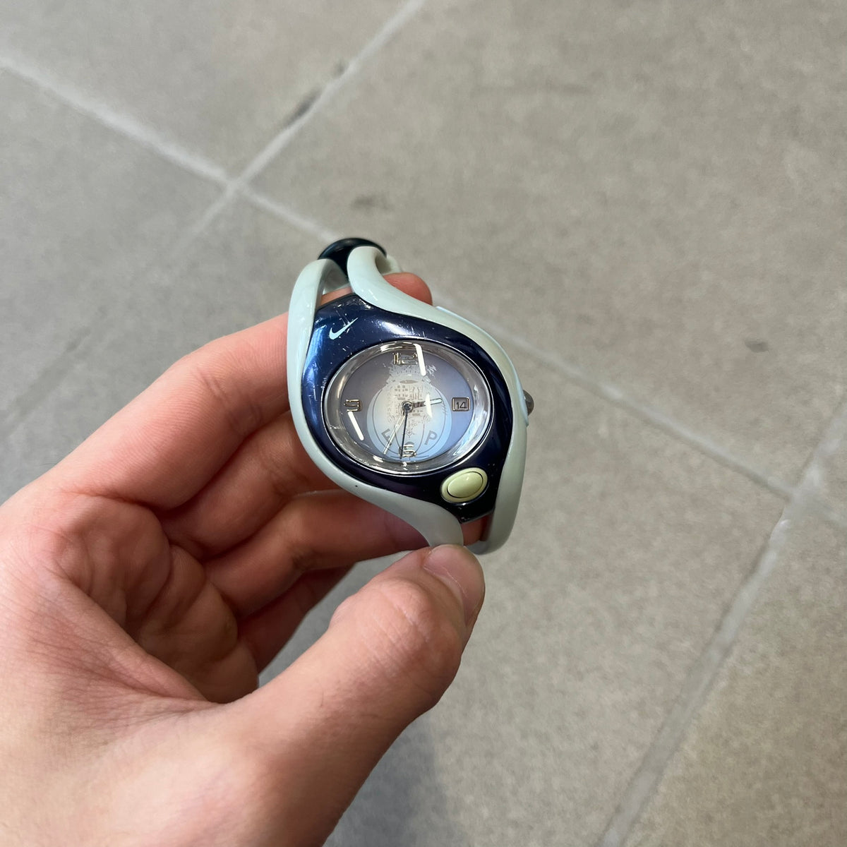 Nike Triax Swift FC Porto WR0078 Analog Watch is an analog sports watch featuring a light blue rubber strap integrated into the case design, forming a one-piece construction. The case is metal navy with a Nike Swoosh at the top and a button used to activate the backlight. The dial is blue and white with the FC Porto football team crest, paired with silver hands. It is water resistant up to 100 meters.