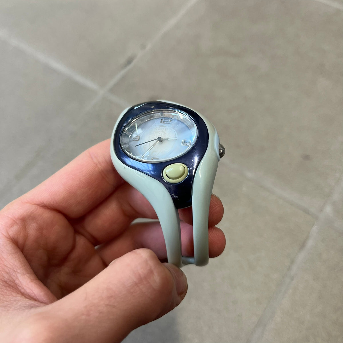 Nike Triax Swift FC Porto WR0078 Analog Watch is an analog sports watch featuring a light blue rubber strap integrated into the case design, forming a one-piece construction. The case is metal navy with a Nike Swoosh at the top and a button used to activate the backlight. The dial is blue and white with the FC Porto football team crest, paired with silver hands. It is water resistant up to 100 meters.