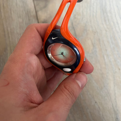 Nike Triax Swift Illinois University WR0078 Analog Watch is a sports watch featuring an integrated one-piece construction with orange straps and navy accents. The dark navy stainless steel case includes a white Nike Swoosh and a white button that activates the light blue backlight. The orange dial features the large Illinois University “I” logo. Made from stainless steel and plastic materials, the watch is water resistant up to 100 meters.