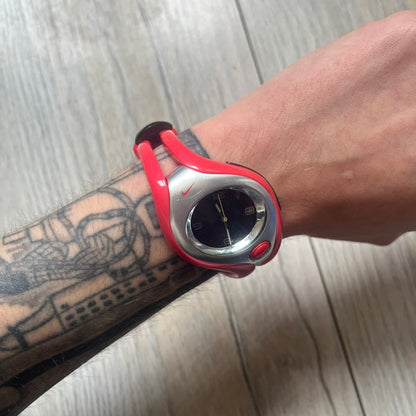 Nike Triax Swift WR0078 analog wristwatch with pink rubber straps and a matching rubber outer case. The internal case is silver-tone metal, fitted with a pink front button and pink Nike Swoosh branding. Features a black dotted dial with silver hands and markers. Sport-oriented construction with a clean, functional layout typical of early-2000s Nike Triax models.