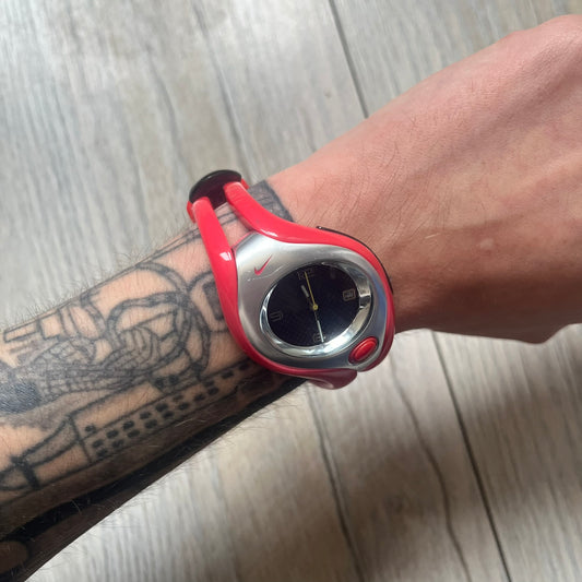 Nike Triax Swift WR0078 analog wristwatch with pink rubber straps and a matching rubber outer case. The internal case is silver-tone metal, fitted with a pink front button and pink Nike Swoosh branding. Features a black dotted dial with silver hands and markers. Sport-oriented construction with a clean, functional layout typical of early-2000s Nike Triax models.