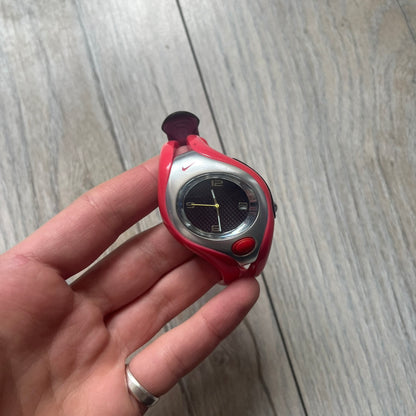 Nike Triax Swift WR0078 analog wristwatch with pink rubber straps and a matching rubber outer case. The internal case is silver-tone metal, fitted with a pink front button and pink Nike Swoosh branding. Features a black dotted dial with silver hands and markers. Sport-oriented construction with a clean, functional layout typical of early-2000s Nike Triax models.