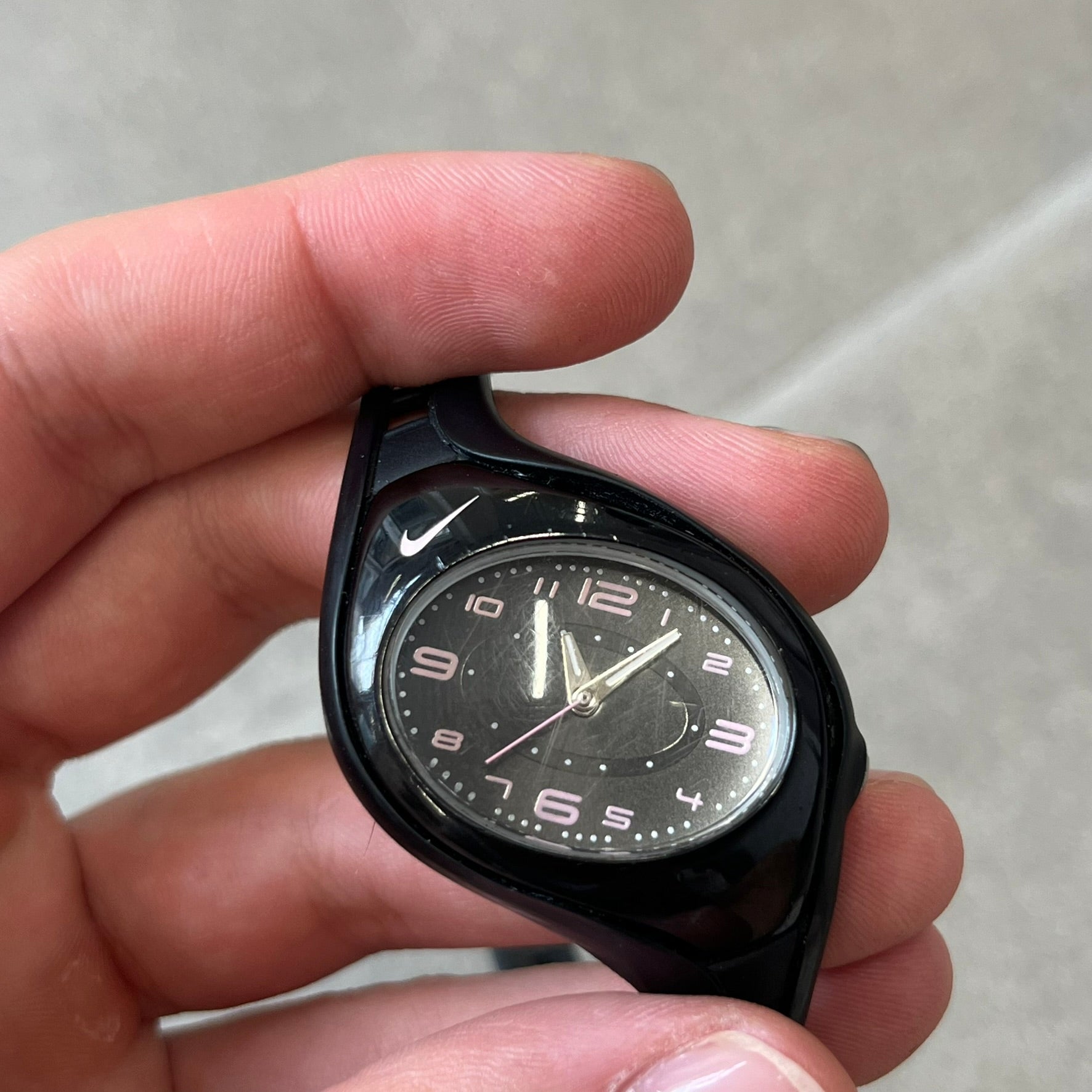Nike Triax Swift WK0007 Black &amp; Pink Analog Watch features a black rubber strap with matching front case. The black dial has pink hour markers, and silver hands. Small Pink Nike logo sits above the case. Built with stainless steel and metal components, the watch is water resistant up to 50 meters.