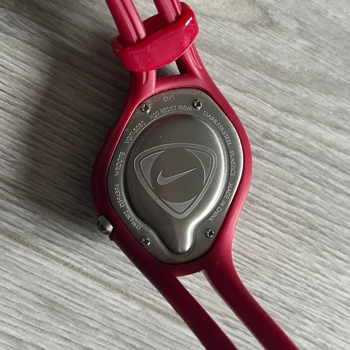 Nike Triax Swift “PSG” WR0078 Analog Watch featuring red rubberized straps and a matching red outer case shell covering the metal housing. The inner case is navy with a white light button and a Nike Swoosh on the side. The dial has a white-to-blue mirrored gradient finish with a large Paris Saint-Germain crest centered on the face, visible depending on light angle. Analog display with an integrated turquoise backlight that illuminates the dial. Designed as an official Nike Triax Swift collaboration tied to 