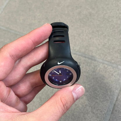 Nike Triax WK0009 Timing Range Blue Analog Watch features a black rubber strap and black rubber case with a silver-tone outline around the dial. The case has a grey Nike Swoosh at the top, while the metallic blue dial features white numerals and black hour markers.
