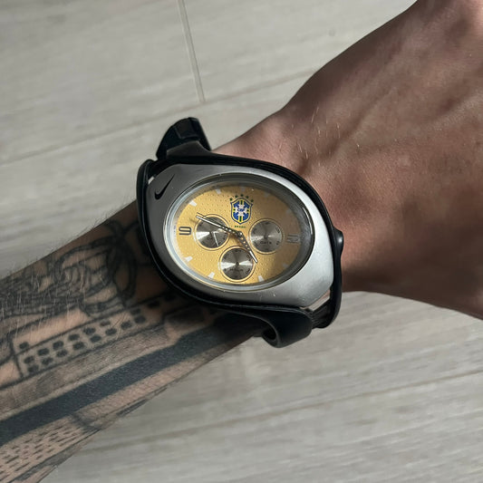Nike Triax “Brasil” Swift 3i WR0091 analog watch with black rubber straps and a silver-tone case featuring a black Nike Swoosh. The yellow metallic dial has a recessed dotted texture, a Brazil crest at the top, three silver subdials for day, date, and hour, silver hands, and a green seconds hand. Seconds markings are printed on the inner edge of the case and are visible only at an angle. Sport-focused Triax case design with water-resistant construction.