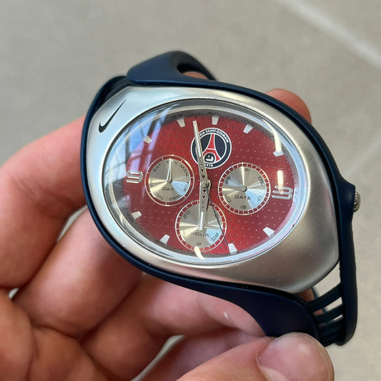 Nike Triax 'PSG' Swift 3i WR0091 Analog Watch with black rubber straps and a silver-tone case featuring a black Nike Swoosh at the top. The red metallic dial has a recessed dotted texture, Paris Saint Germain crest at the top and three silver subdials for day, date, and hour. Seconds markings are printed on the inner edge of the case and are visible only at an angle.&nbsp;