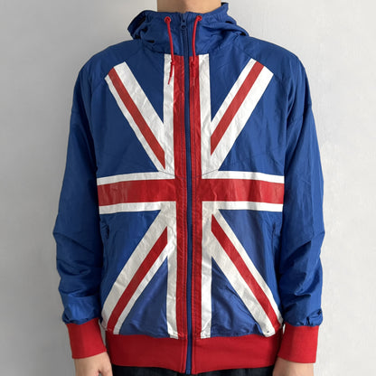 Nike UK Olympics 2008 Split Windbreaker designed by Jarrett Reynolds. Features a blue base with Union Jack-inspired red and white stripes on the front, representing Great Britain. Dual side zippers allow the jacket to be split in half and combined with other pieces from the collection, with a subtle United Kingdom flags inside the pocket.