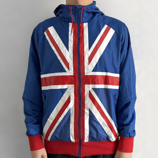 Nike UK Olympics 2008 Split Windbreaker designed by Jarrett Reynolds. Features a blue base with Union Jack-inspired red and white stripes on the front, representing Great Britain. Dual side zippers allow the jacket to be split in half and combined with other pieces from the collection, with a subtle United Kingdom flags inside the pocket.