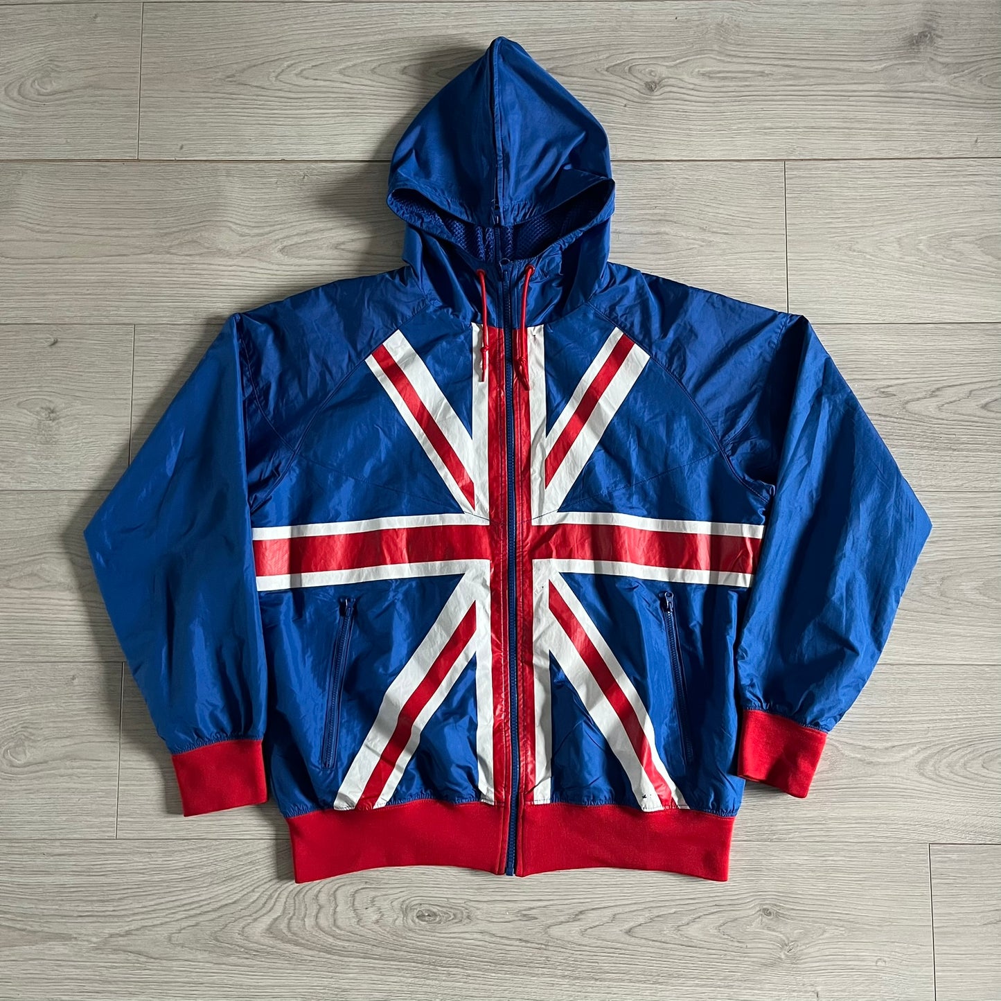 Nike UK Olympics 2008 Split Windbreaker designed by Jarrett Reynolds. Features a blue base with Union Jack-inspired red and white stripes on the front, representing Great Britain. Dual side zippers allow the jacket to be split in half and combined with other pieces from the collection, with a subtle United Kingdom flag inside the pocket.