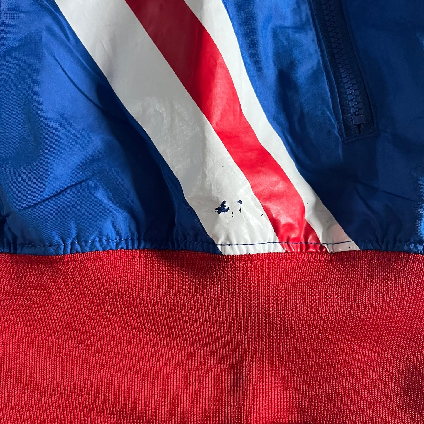 Nike UK Olympics 2008 Split Windbreaker designed by Jarrett Reynolds. Features a blue base with Union Jack-inspired red and white stripes on the front, representing Great Britain. Dual side zippers allow the jacket to be split in half and combined with other pieces from the collection, with a subtle United Kingdom flag inside the pocket.