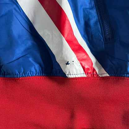 Nike UK Olympics 2008 Split Windbreaker designed by Jarrett Reynolds. Features a blue base with Union Jack-inspired red and white stripes on the front, representing Great Britain. Dual side zippers allow the jacket to be split in half and combined with other pieces from the collection, with a subtle United Kingdom flag inside the pocket.