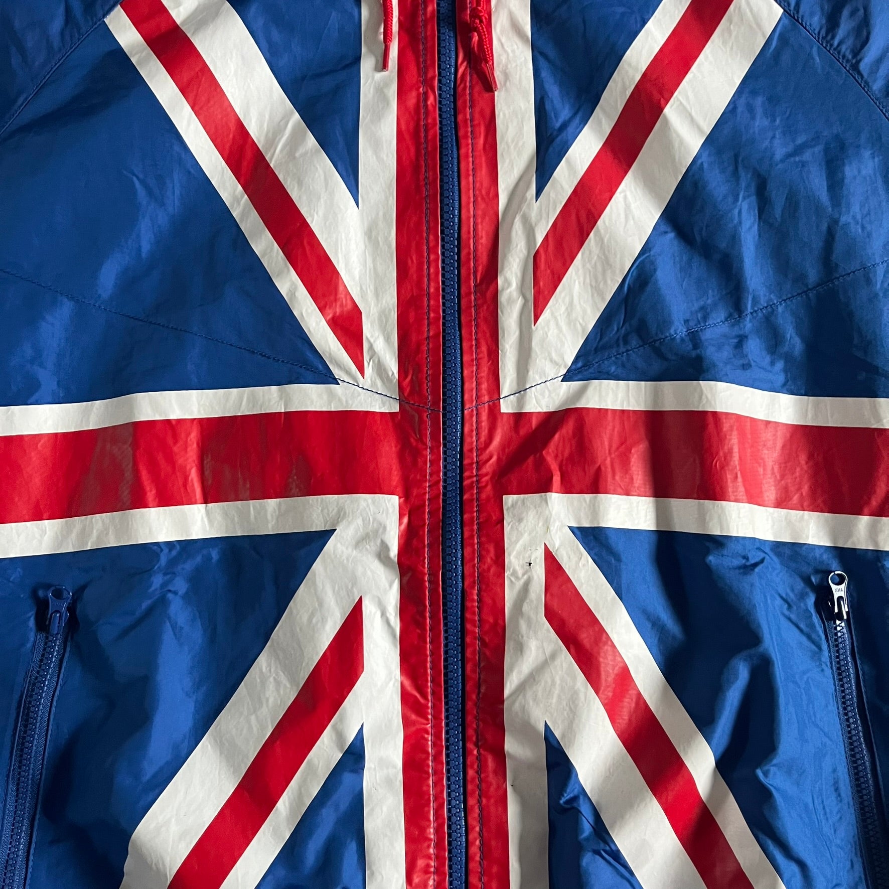Nike UK Olympics 2008 Split Windbreaker designed by Jarrett Reynolds. Features a blue base with Union Jack-inspired red and white stripes on the front, representing Great Britain. Dual side zippers allow the jacket to be split in half and combined with other pieces from the collection, with a subtle United Kingdom flag inside the pocket.