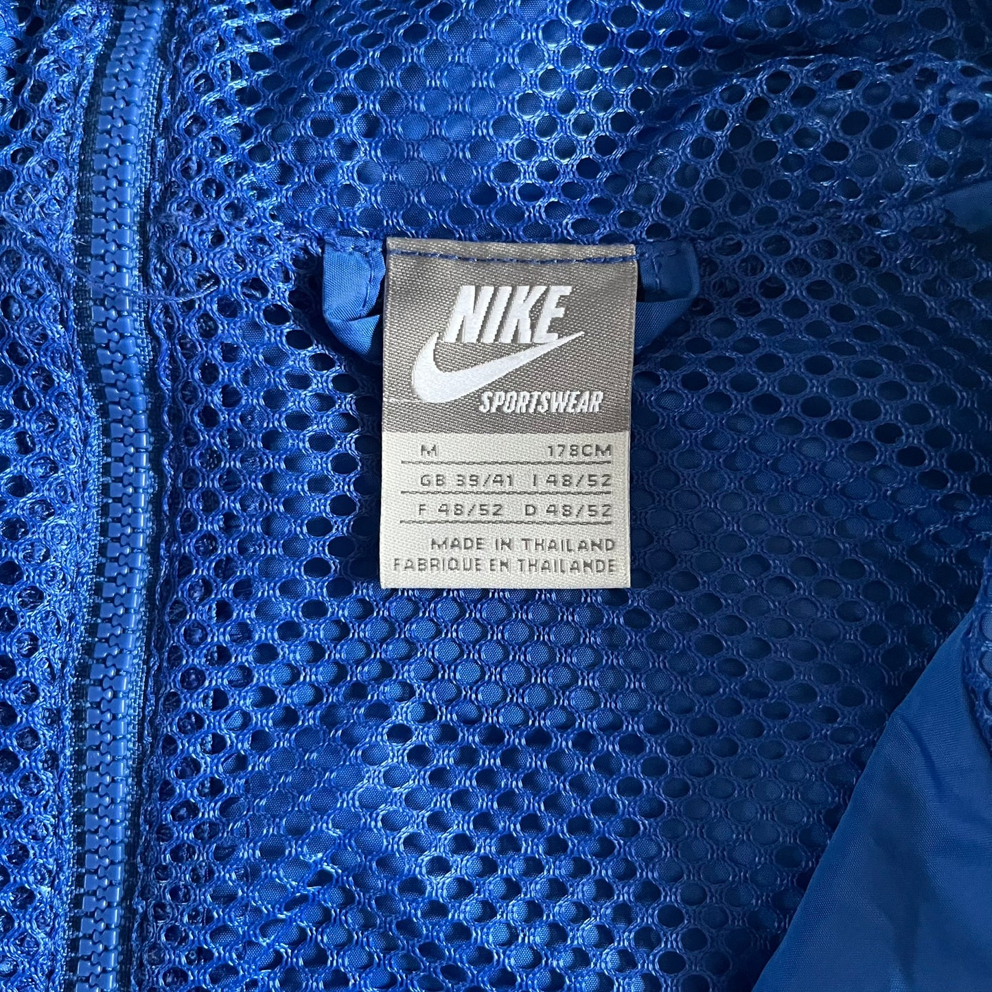 Nike UK Olympics 2008 Split Windbreaker designed by Jarrett Reynolds. Features a blue base with Union Jack-inspired red and white stripes on the front, representing Great Britain. Dual side zippers allow the jacket to be split in half and combined with other pieces from the collection, with a subtle United Kingdom flag inside the pocket.