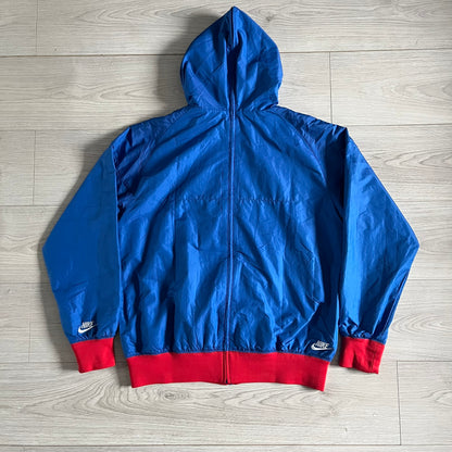 Nike UK Olympics 2008 Split Windbreaker designed by Jarrett Reynolds. Features a blue base with Union Jack-inspired red and white stripes on the front, representing Great Britain. Dual side zippers allow the jacket to be split in half and combined with other pieces from the collection, with a subtle United Kingdom flag inside the pocket.