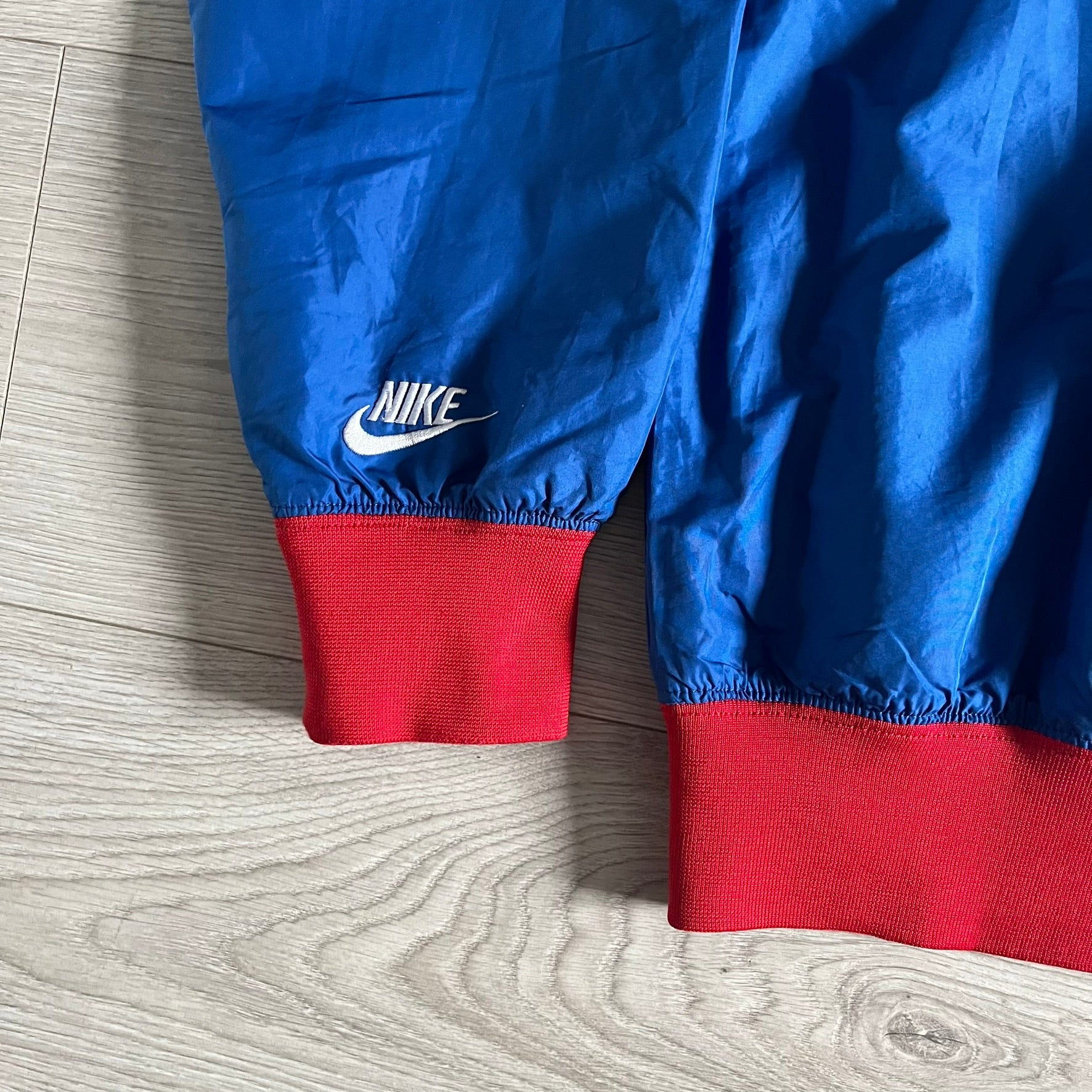 Nike UK Olympics 2008 Split Windbreaker designed by Jarrett Reynolds. Features a blue base with Union Jack-inspired red and white stripes on the front, representing Great Britain. Dual side zippers allow the jacket to be split in half and combined with other pieces from the collection, with a subtle United Kingdom flag inside the pocket.