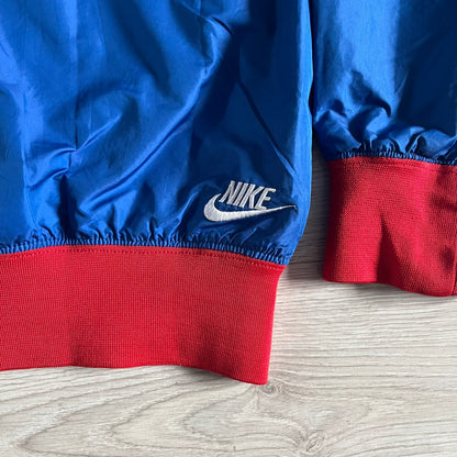 Nike UK Olympics 2008 Split Windbreaker designed by Jarrett Reynolds. Features a blue base with Union Jack-inspired red and white stripes on the front, representing Great Britain. Dual side zippers allow the jacket to be split in half and combined with other pieces from the collection, with a subtle United Kingdom flag inside the pocket.