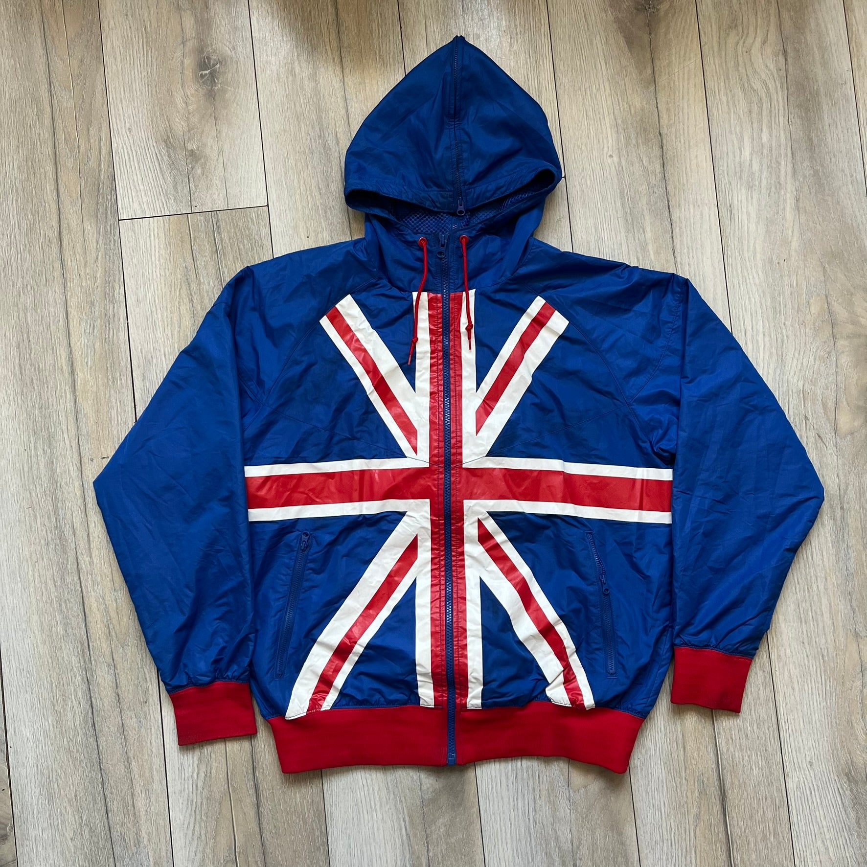 Nike UK Olympics 2008 Split Windbreaker designed by Jarrett Reynolds. Features a blue base with Union Jack-inspired red and white stripes on the front, representing Great Britain. Dual side zippers allow the jacket to be split in half and combined with other pieces from the collection, with a subtle United Kingdom flags inside the pocket.